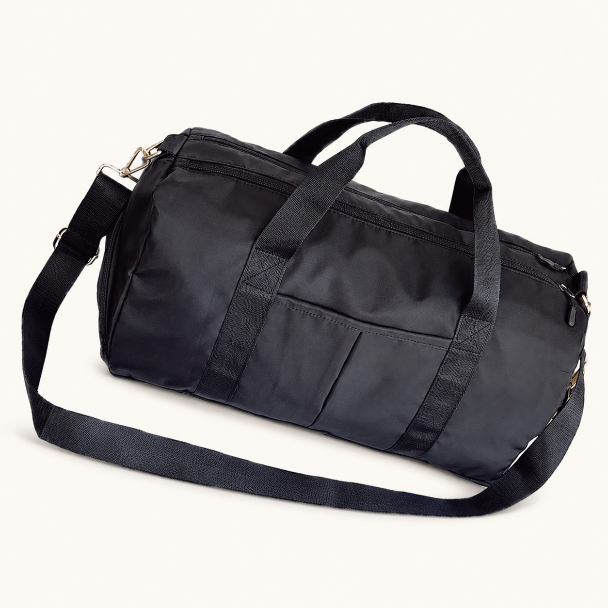 Black Split Duffel Bag with carry handles, shoulder strap and front slip pockets on a warm off-white studio background.