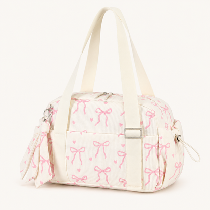 Cream mini gym bag with pink bow print, long carry handles, front pocket and side pockets on a warm off-white background.