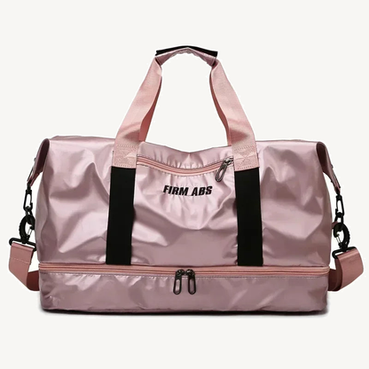 Pearlescent pink fitness duffel with black webbing, detachable shoulder strap, front zip pocket and lower zip compartment on a warm off-white background.