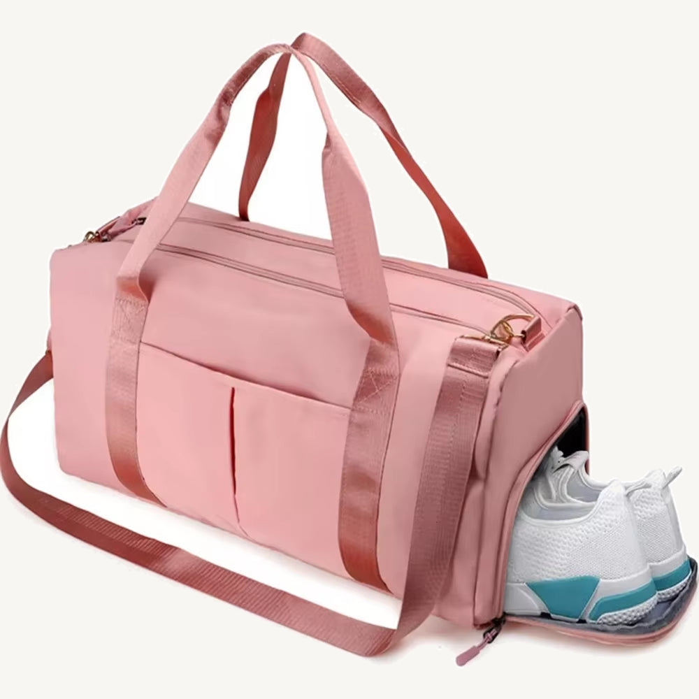 Pink split duffel with two carry handles, shoulder strap, front slip pockets and an open side compartment holding white shoes on a warm off-white background.