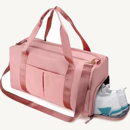 Pink split duffel with two carry handles, shoulder strap, front slip pockets and an open side compartment holding white shoes on a warm off-white background.