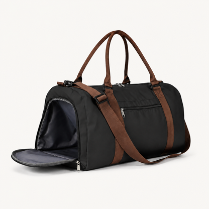 Black duffel with brown carry handles and shoulder strap, front zip pocket and open side compartment on a warm off-white background.